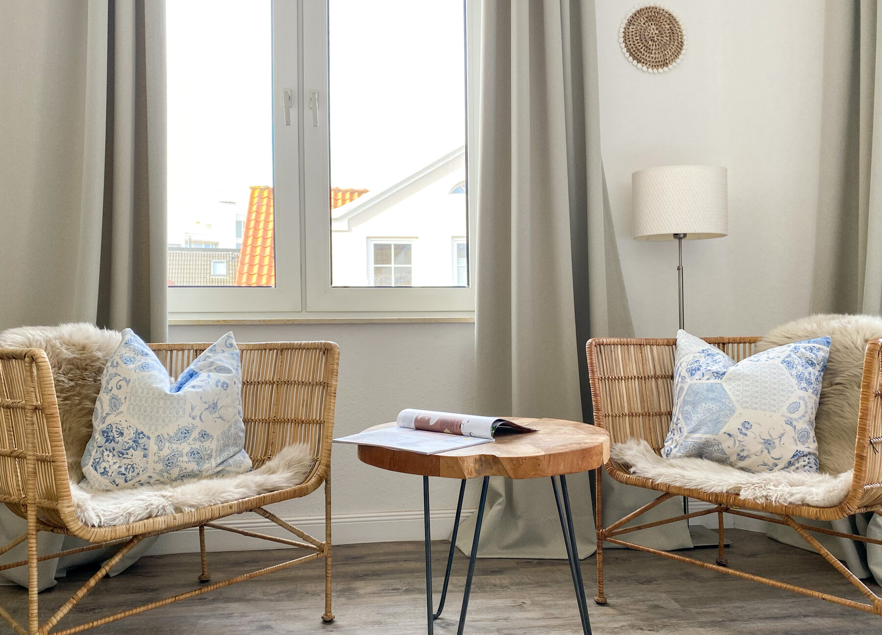 Zwei Rattan-Sessel mit Fell und blau-weißen Kissen am Fenster